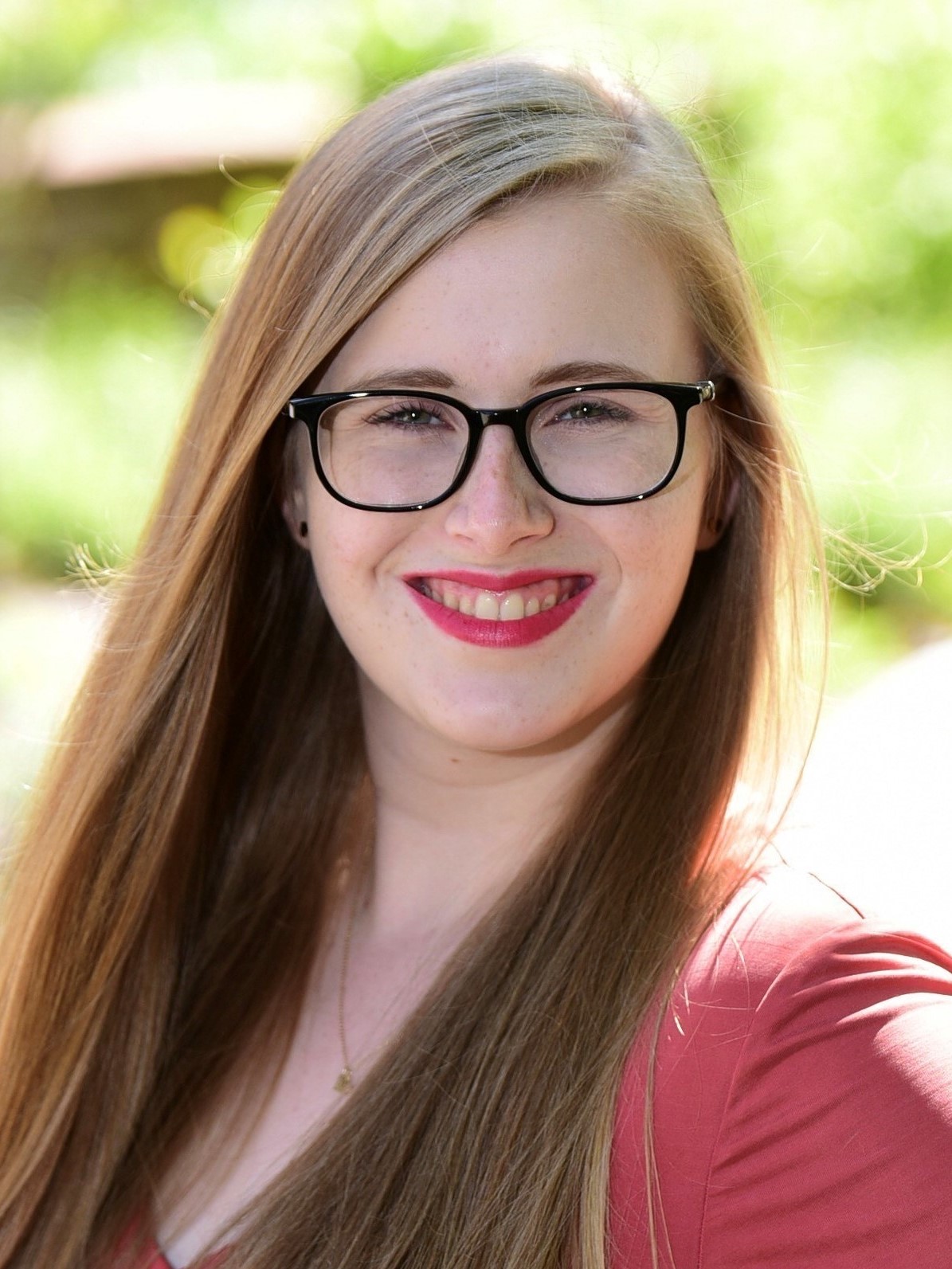 Photo of Katie Adler with long blonde hair smiling glasses and orange blouse